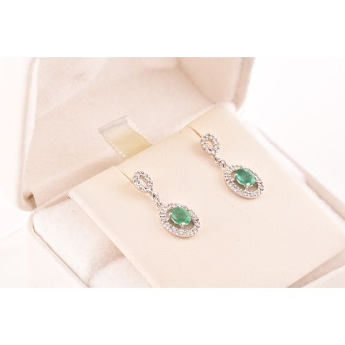 53 - A pair of 18ct white gold emerald and diamond drop earrings, each set with an oval cut emerald with ... 