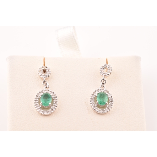 53 - A pair of 18ct white gold emerald and diamond drop earrings, each set with an oval cut emerald with ... 