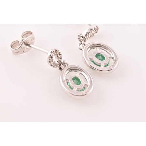 53 - A pair of 18ct white gold emerald and diamond drop earrings, each set with an oval cut emerald with ... 