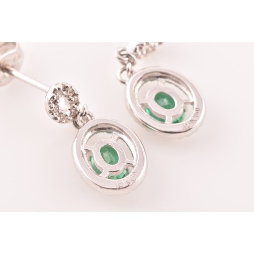 53 - A pair of 18ct white gold emerald and diamond drop earrings, each set with an oval cut emerald with ... 