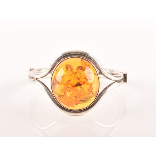 108 - A silver and amber bangle bracelet, set with a large oval cabochon amber, measuring approximately 3.... 