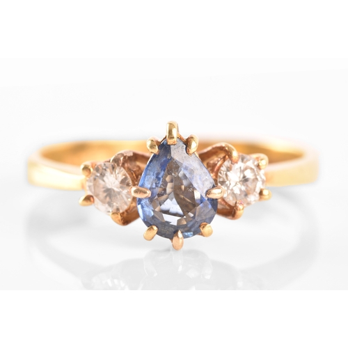 96 - A 18ct yellow gold three stone ring, featuring a pear cut blue stone to the centre, flanked by two r... 