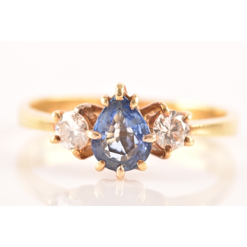 96 - A 18ct yellow gold three stone ring, featuring a pear cut blue stone to the centre, flanked by two r... 