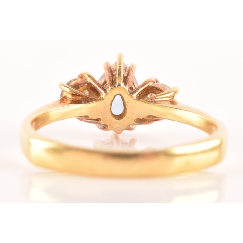 96 - A 18ct yellow gold three stone ring, featuring a pear cut blue stone to the centre, flanked by two r... 