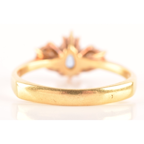 96 - A 18ct yellow gold three stone ring, featuring a pear cut blue stone to the centre, flanked by two r... 