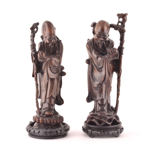 241 - A pair of mid-20th century Chinese carved wood figurines, each depicting an elderly figure holding a... 