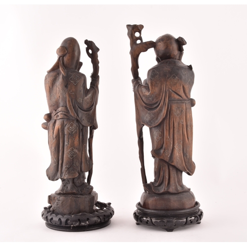 241 - A pair of mid-20th century Chinese carved wood figurines, each depicting an elderly figure holding a... 