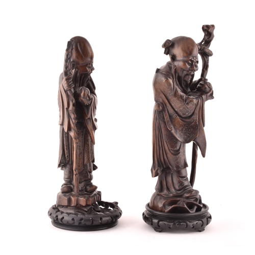 241 - A pair of mid-20th century Chinese carved wood figurines, each depicting an elderly figure holding a... 