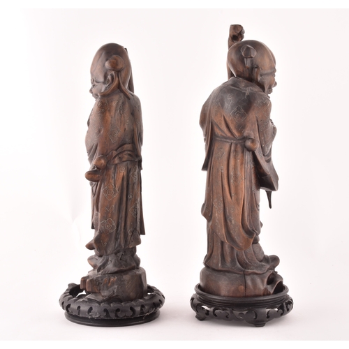 312 - A pair of mid-20th century Chinese carved wood figurines, each depicting an elderly figure holding a... 