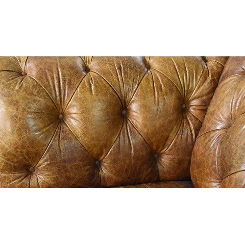 382 - A large brown leather button back Chesterfield style sofa, supported on turned wooden legs, 229 cm w... 