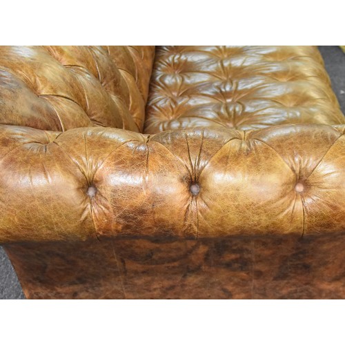 382 - A large brown leather button back Chesterfield style sofa, supported on turned wooden legs, 229 cm w... 