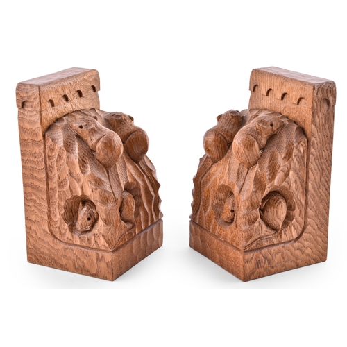 Robert 'Mouseman' Thompson, a rare and unusual pair of triple mice adzed oak book ends, honey coloured and of angular form, with arcaded tops above curved sides, each with two climbing mice and one beneath appearing through side holes, 18 cm high, 10 cm wide, 10 cm deep.