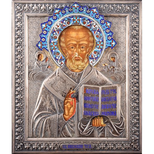 A fine Russian Imperial silver and cloisonné enamel oklad icon of St Nicholas, Moscow, 1893, by Ivan Khlebnikov, the oklad struck with maker’s mark И.П. ХЛЕБНИКОВЪ, Moscow town mark, and 84 zolotniki standard, the saint shown half-length blessing and holding the Gospel, flanked by Christ and the Mother of God issuing from clouds, the whole enclosed within a richly engraved silver ground and border, and surmounted by an outstanding shaded-enamel halo worked in blues, whites, reds and turquoise; the original painted panel visible through the apertures, with age craquelure and small losses; the reverse plain. 31.5 x 27 cm.