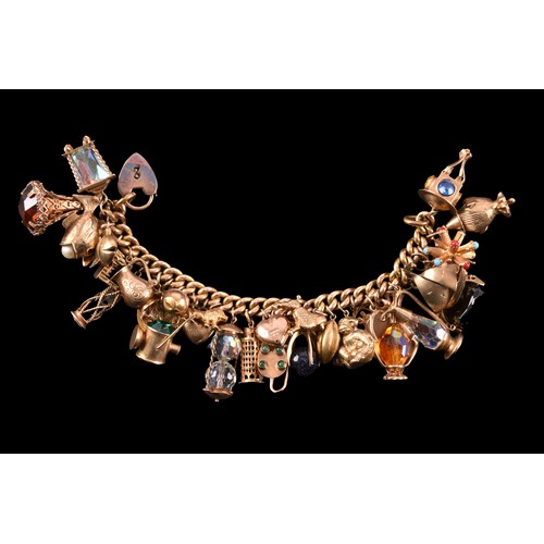 A heavy yellow gold curb link charm bracelet, suspended with 9ct, 18ct, and unmarked charms, 32 charms in total, 16.5 cm long.