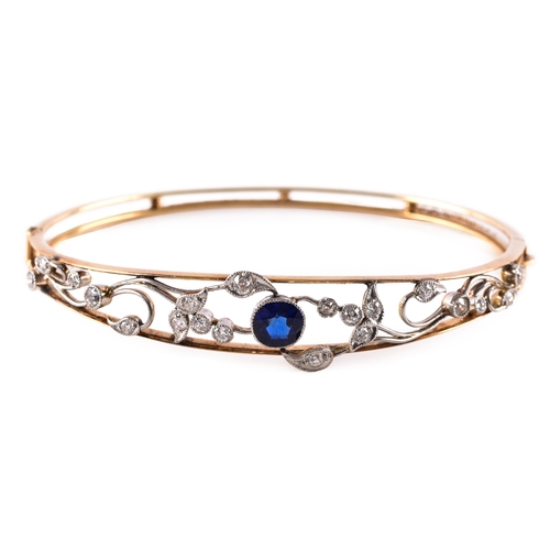 34 - A yellow gold and platinum bangle, set to the centre with a cushion shape synthetic sapphire with an... 