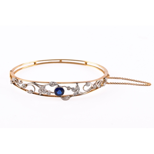 34 - A yellow gold and platinum bangle, set to the centre with a cushion shape synthetic sapphire with an... 