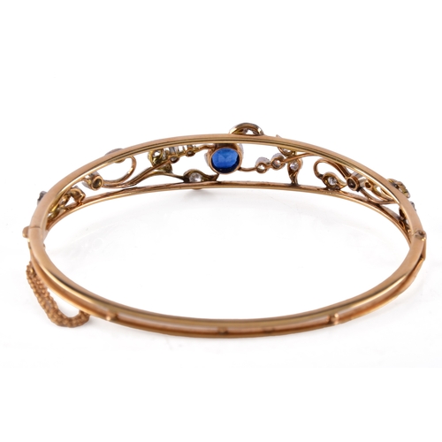 34 - A yellow gold and platinum bangle, set to the centre with a cushion shape synthetic sapphire with an... 