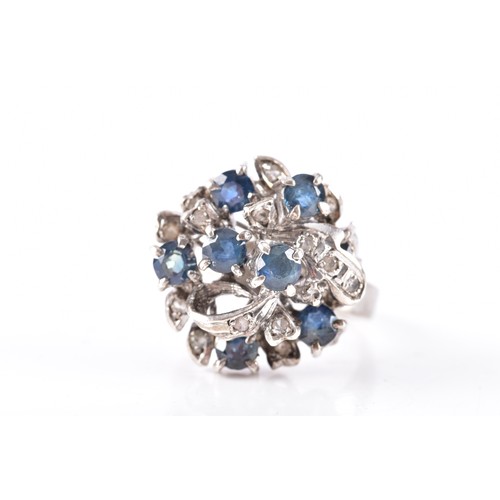 66 - A white metal, sapphire, and white paste stone cluster ring, the ribbon twist mount set with six mix... 
