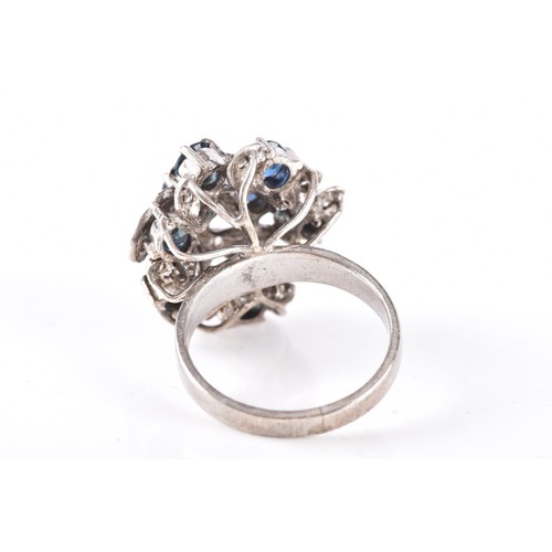 66 - A white metal, sapphire, and white paste stone cluster ring, the ribbon twist mount set with six mix... 