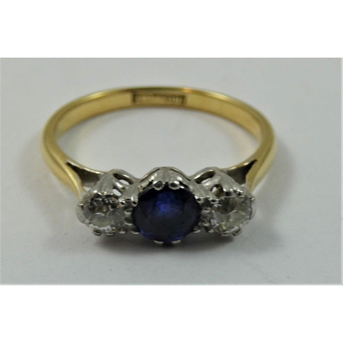 74 - An 18 ct gold sapphire and diamond three stone ring, claw set with an oval mixed cut stone flanked b... 