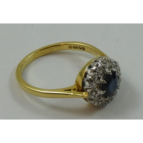 77 - An 18ct gold sapphire and diamond cluster ring, claw set with a mixed cut stone, bordered by single ... 