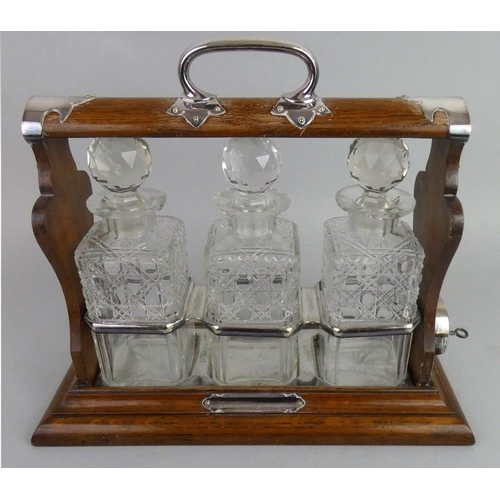 130 - An Edwardian oak three bottle Tantalus, containing hob nail cut bottles, with electroplated mounts, ... 