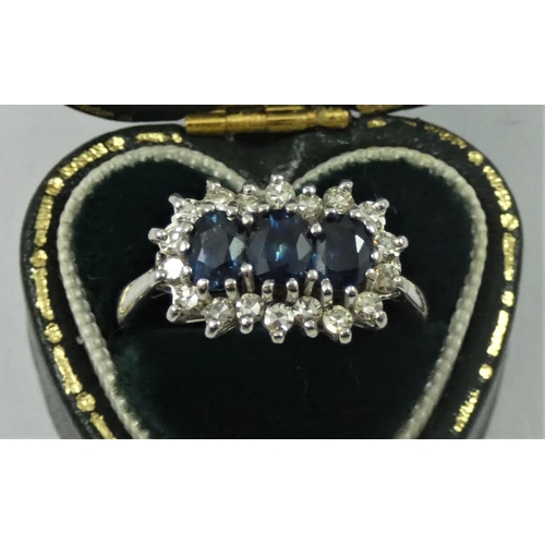 85 - An 18ct white gold sapphire and diamond three stone ring, the oval mixed cut stones bordered by sing... 