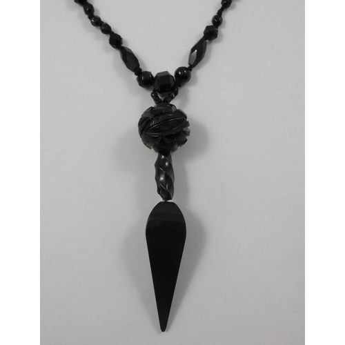 116 - A Victorian jet longchain, the tapering pear shape drop with carved bead above to a long length of f... 