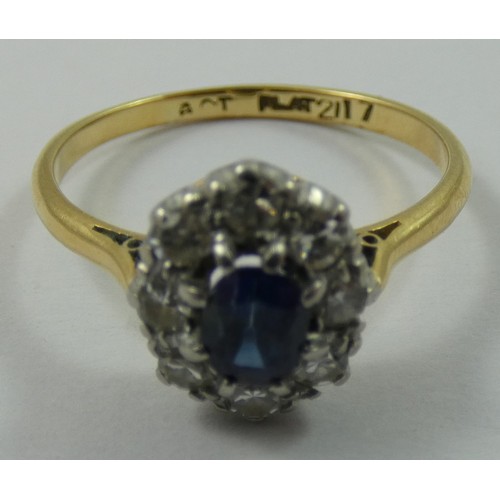 126 - An 18ct gold sapphire and diamond cluster ring, claw set with an oval mixed cut stone, bordered by e... 