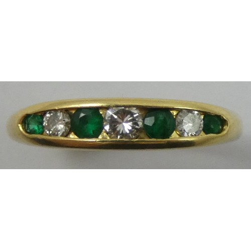 149 - An 18ct gold emerald and diamond seven stone ring, channel set with graduated brilliant cut stones, ... 