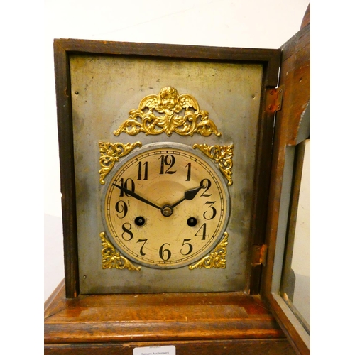 87 - An oak cased manual wind mantle clock with arched and carved pediment. 38cm tall.