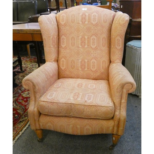 445 - A pink upholstered wingback armchair, raised on tapering legs with brass castors and a stained beech... 