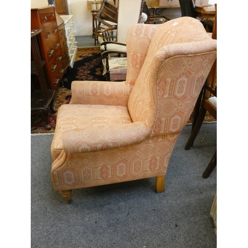 445 - A pink upholstered wingback armchair, raised on tapering legs with brass castors and a stained beech... 