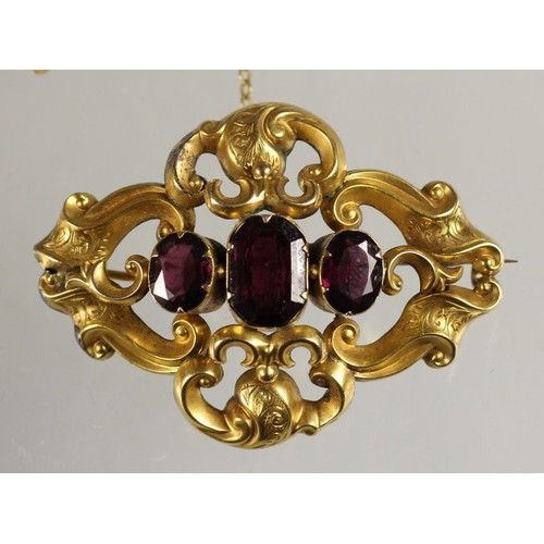 85 - A Victorian gold and garnet brooch, set with three graduated mixed cut stones  within an openwork sc... 