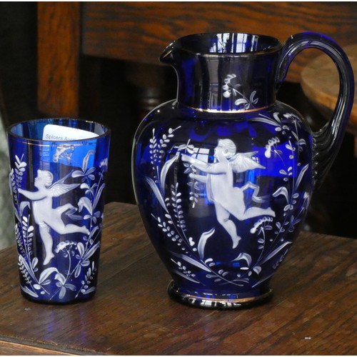 110 - A cobalt blue glass jug with white cherub decoration together with a matching drinking glass
