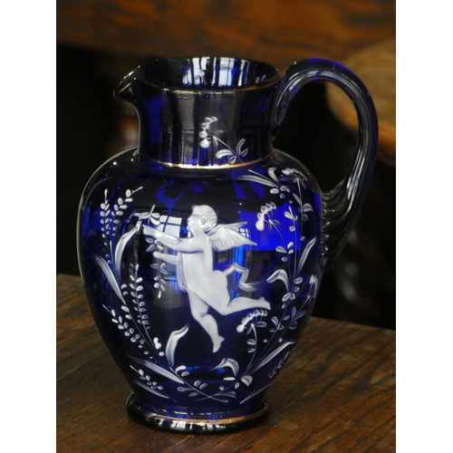 110 - A cobalt blue glass jug with white cherub decoration together with a matching drinking glass