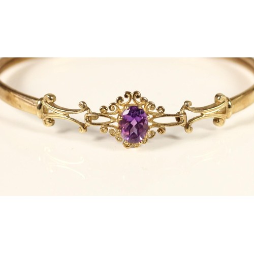 85 - A 9ct gold Victorian style sprung bangle, the scroll front set with a mixed cut amethyst, 6.2gm