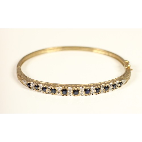 106 - A Victorian style 9ct gold sapphire and diamond hinged bangle, carved claw set with mixed cut stones... 