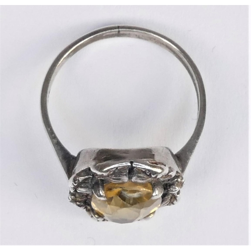 131 - An Arts & Crafts silver and citrine ring, calw set with a mixed cut stone, floral frame, size L 1/2.