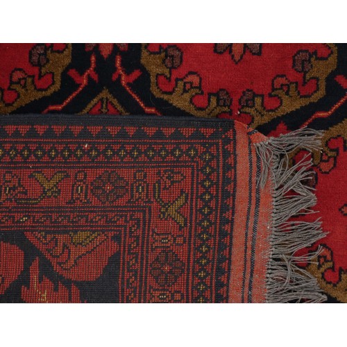 218 - A Turkish woollen Bokhara rug, having a red ground with blue guls, 350 x 250cm