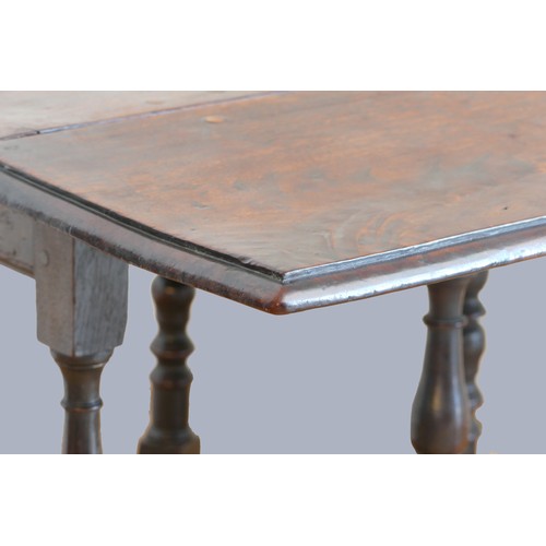 320 - A 17th century red walnut gateleg table, with plank top, the oak base with turned baluster legs and ... 