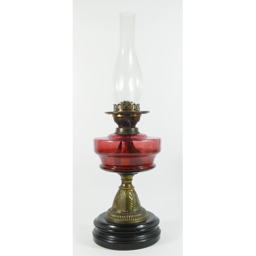 295 - Victorian brass oil lamp with cranberry glass globe, raised on a ceramic base - 58cm tall.