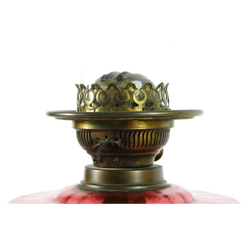 295 - Victorian brass oil lamp with cranberry glass globe, raised on a ceramic base - 58cm tall.