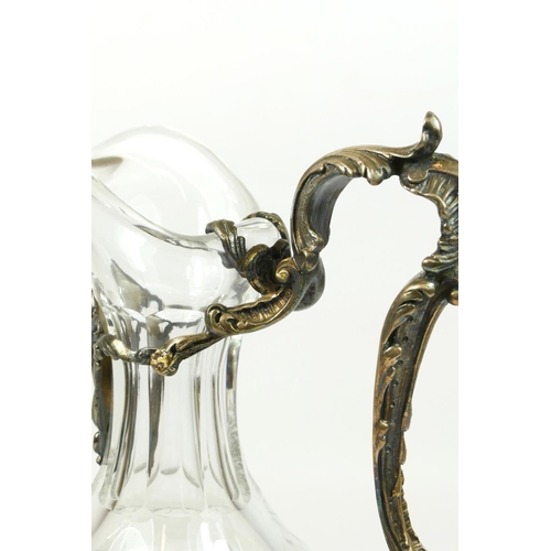 29 - An electroplated and cut glass wine ewer, the cutglass body with floral scroll handle and scroll fee... 