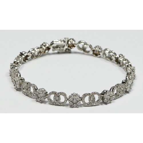 89 - A 14K white gold and diamond line bracelet, claw set with 12 brilliant cut diamond set clusters, wit... 