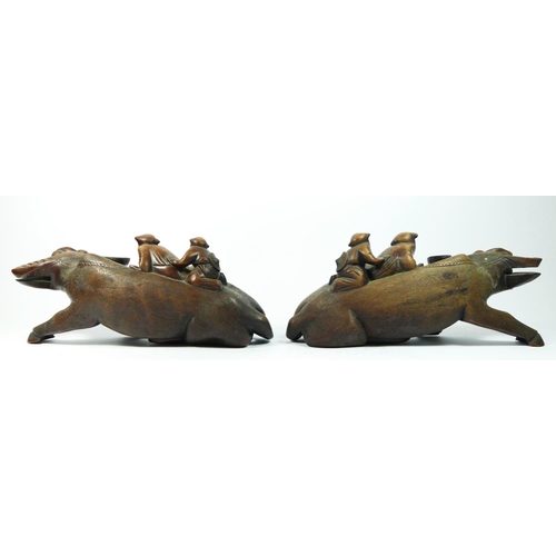 257 - A Chinese pair of carved hardwood recumbent water buffalo with two riders, glass eyes, 36 x 15cm.