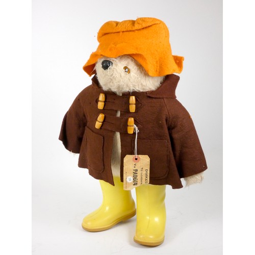 A Paddington bear teddy, c.1972, made by Gabrielle, in felt orange rain cap, felt duffle coat with wooden toggles and yellow plastic wellies, with rail tag