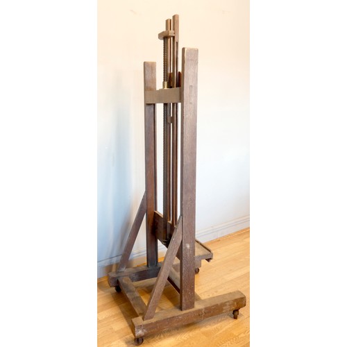 393 - An early 20th century oak studio easel, the 'H' frame with bevel gear mechanism, with shelf and adju... 