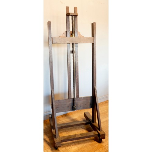 393 - An early 20th century oak studio easel, the 'H' frame with bevel gear mechanism, with shelf and adju... 