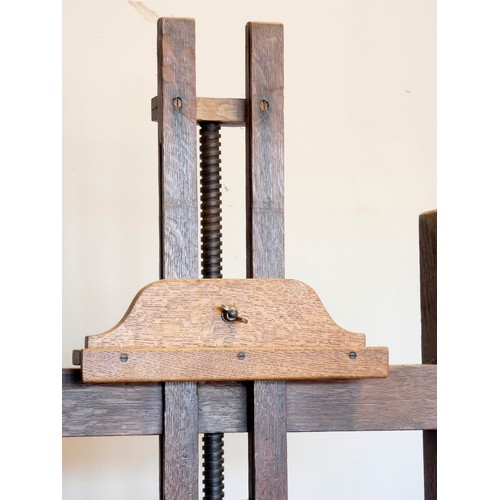 393 - An early 20th century oak studio easel, the 'H' frame with bevel gear mechanism, with shelf and adju... 